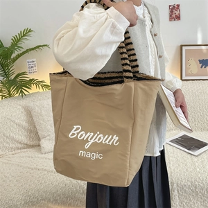 Detail of khaki tote bag with plush striped handles and Bonjour magic slogan lettering