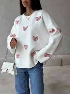 White knit sweater with red heart embroidery, long sleeves, and casual crewneck design