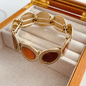 Elastic gold metal bracelet with leopard print resin discs in a wooden jewelry box
