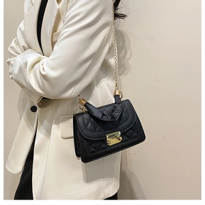 Bolso bandolera acolchado negro con cadena dorada y asa plisada sobre una modelo