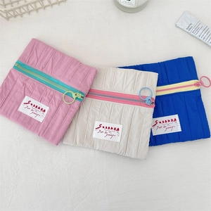 Detailed view of three pleated makeup bags in pink, beige and blue with ring zippers