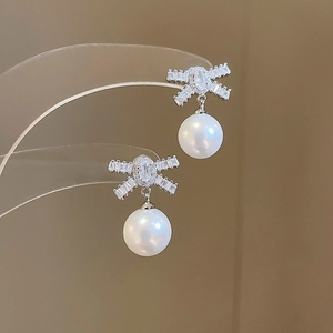 Detailed view of silver bow-shaped earrings with sparkling cubic zirconia and white pearl drop