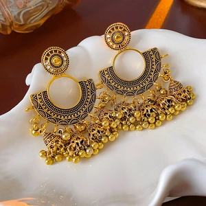 Detailed close-up of golden vintage Jhumka earrings with bells on a white ceramic tray