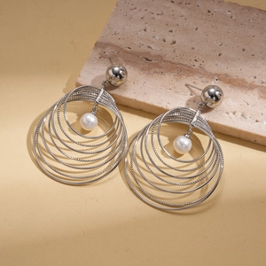 Macro detail of silver layered hoops earring with a white pearl on a textured stone