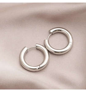 Detailed view of polished silver hoop earrings on elegant pink silk fabric texture