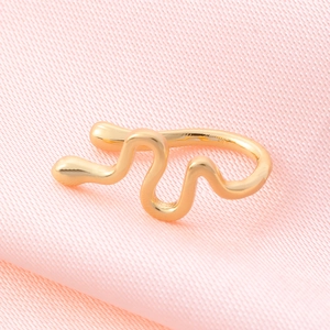 Macro shot of gold wave-shaped ear cuff with metallic texture on pink silk fabric