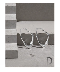 Macro shot of irregular geometric S925 silver hoop earrings on a stone textured background