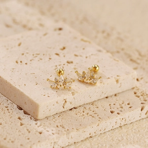 Detailed close-up of gold crown stud earrings with clear zircon stones on a stone slab