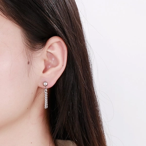 Detail of silver tassel chain earrings on ear, featuring a minimalist round stud and chain