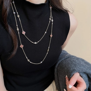 Detail of a layered gold necklace with pink flower charms and pearls on a model