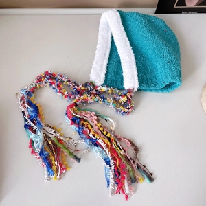 Detail of teal knit hat with white faux fur trim and long colorful braided tassels