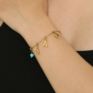 Détail d'un bracelet doré avec étoile de mer, breloques cœur et perle turquoise bleue