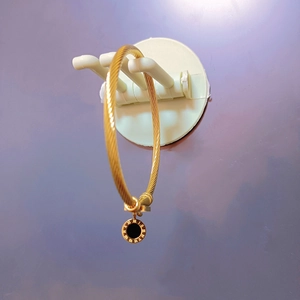 Detailed macro view of gold twisted wire bracelet with Roman numeral black enamel charm