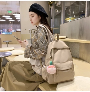 Detail view of beige backpack side pocket with a pink plush peach charm attached