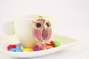 Macro detail of golden owl keychain with pink enamel scales and crystal embellishments