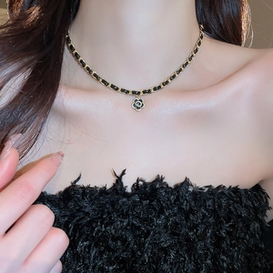 Close-up of gold-plated camellia pendant on a black leather interwoven chain necklace