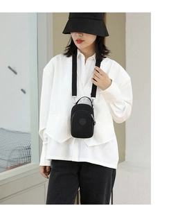 Detail of a black nylon mini crossbody bag with multi-layer zippers on a stylish model