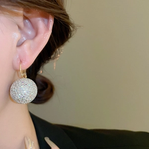 Close-up of elegant gold hoop earrings with large sparkling crystal-studded spheres on a model