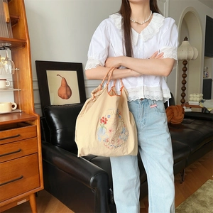 Broderie détaillée sur un sac fourre-tout en toile beige avec anses à carreaux