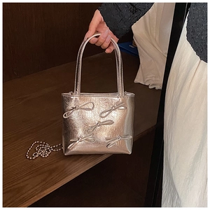 Detail of silver metallic mini square bag featuring a decorative bow and chain strap