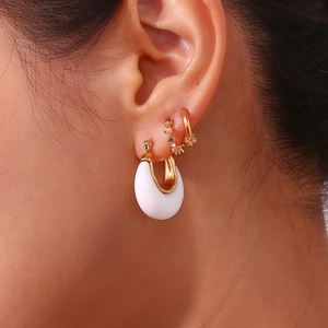 Close-up of white enamel C-shaped earring and gold studs with gemstones on ear