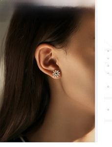 Close-up of small daisy stud earrings in white enamel and gold worn by a model