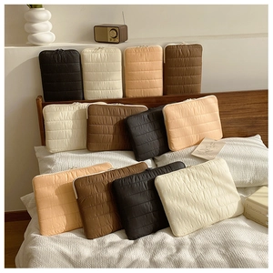 Quilted laptop sleeves in black, cream, apricot and brown on a cozy bedroom background
