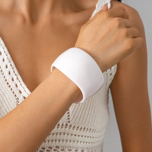 Close-up of a wide matte white resin cuff bracelet worn with a white crochet top