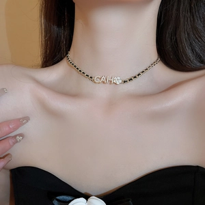 Detail of black and gold woven chain necklace with camellia flower and CAH letter pendant