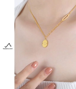 Detail of gold-plated stainless steel necklace with Good Luck pendant on white knitwear