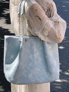 Light blue ice-textured tote bag with chain strap shown on a model in a street setting