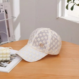Casquette de baseball en dentelle blanche avec logo M doré sur une table en bois