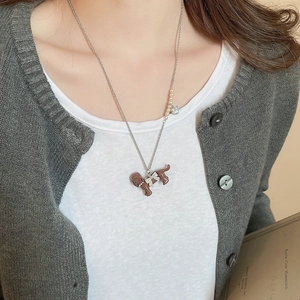Close-up of a silver chain necklace featuring a brown puppy pendant with a pearl detail