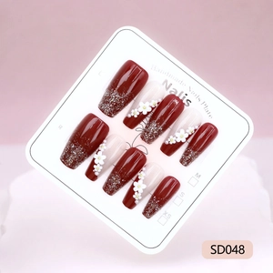 Faux ongles faits main avec dégradé pailleté rouge et fleurs 3D blanches sur carte