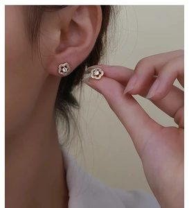 Detailed view of a gold flower earring with micro-pave zircons worn on earlobe
