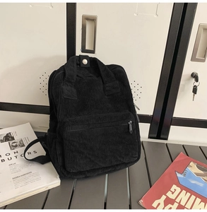 Detail eines schwarzen Cord-Minirucksacks mit Druckknopfgriffen und Reißverschlusstasche