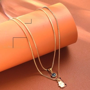 Detail of Hamsa Hand and Evil Eye pendants on a golden double-layered necklace