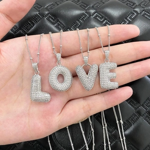 Silver LOVE letter necklace with white zircon stones held against black leather