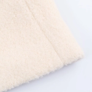 Close-up of beige bouclé fabric texture showing soft curly fleece and wool material