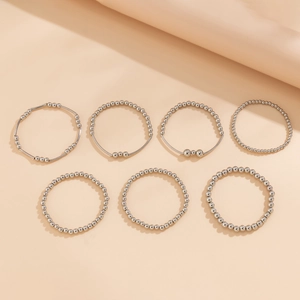 Detail of 7-piece silver beaded metal bracelet set with heart pendants on beige background
