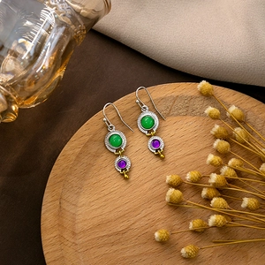 Detailed view of vintage silver earrings with green and purple gems on a wooden tray