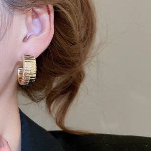 Macro detail of gold-tone C-shape hoop earrings featuring a unique ribbed texture finish