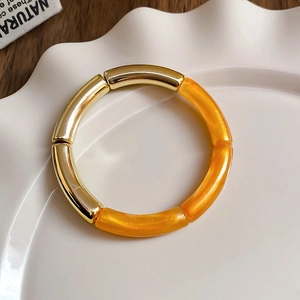 Detail of minimalist gold and orange resin segmented bangle on a white ceramic tray