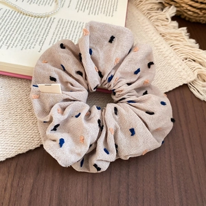 Close-up of beige fabric scrunchie with colorful dots embroidery on a rustic table