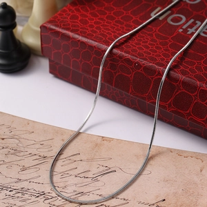 Silver snake chain necklace draped on a red box and vintage paper with chess pieces