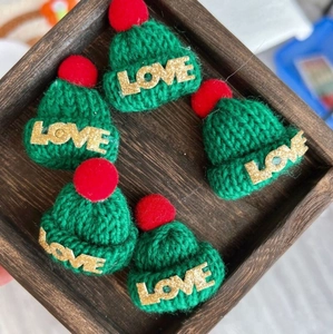Five green mini knitted Christmas hats with red pom-poms and gold LOVE lettering