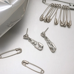 Macro shot of silver safety pin earrings with heart studs and cubic zirconia accents