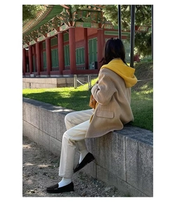 Model wearing a camel wool coat and yellow hoodie in a scenic autumn outdoor setting