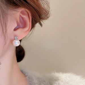 Close-up of a silver needle pearl earring with zircon gemstone on a model's ear