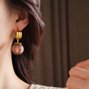 Close-up of elegant gold hoop earrings with a translucent dusty pink resin ball pendant